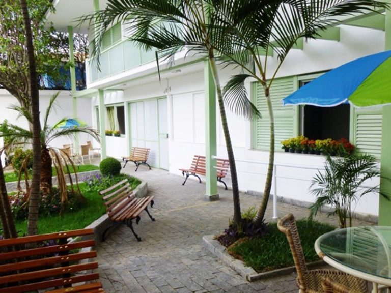 muito verde, bancos de jardim, mesas e cadeiras na área externa