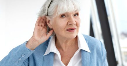 Mulher idosa elegante com problemas auditivos coloca a mão na orelha tentando escutar